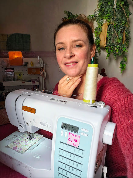 la créatrice de mon fil à passion assise à son atelier derrière sa machine à coudre. une ambiance cocooning et chaleureuse avec la créatrice tout sourire