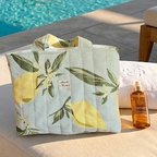 Cabas vert pâle aux motifs citron. Posé sur un transat au bord d'une piscine dans un hotel de luxe. Une crème solaire et une serviette accompagne le cabas matellassé Mon Fil à Passion 