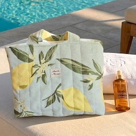 Cabas vert pâle aux motifs citron. Posé sur un transat au bord d'une piscine dans un hotel de luxe. Une crème solaire et une serviette accompagne le cabas matellassé Mon Fil à Passion 