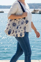 Grand sac cabas avec des motifs namasté main protectrice, lune et soleil. Le grand sac fourre tout est porté a l'épaule d'une femme se baladant dans un port