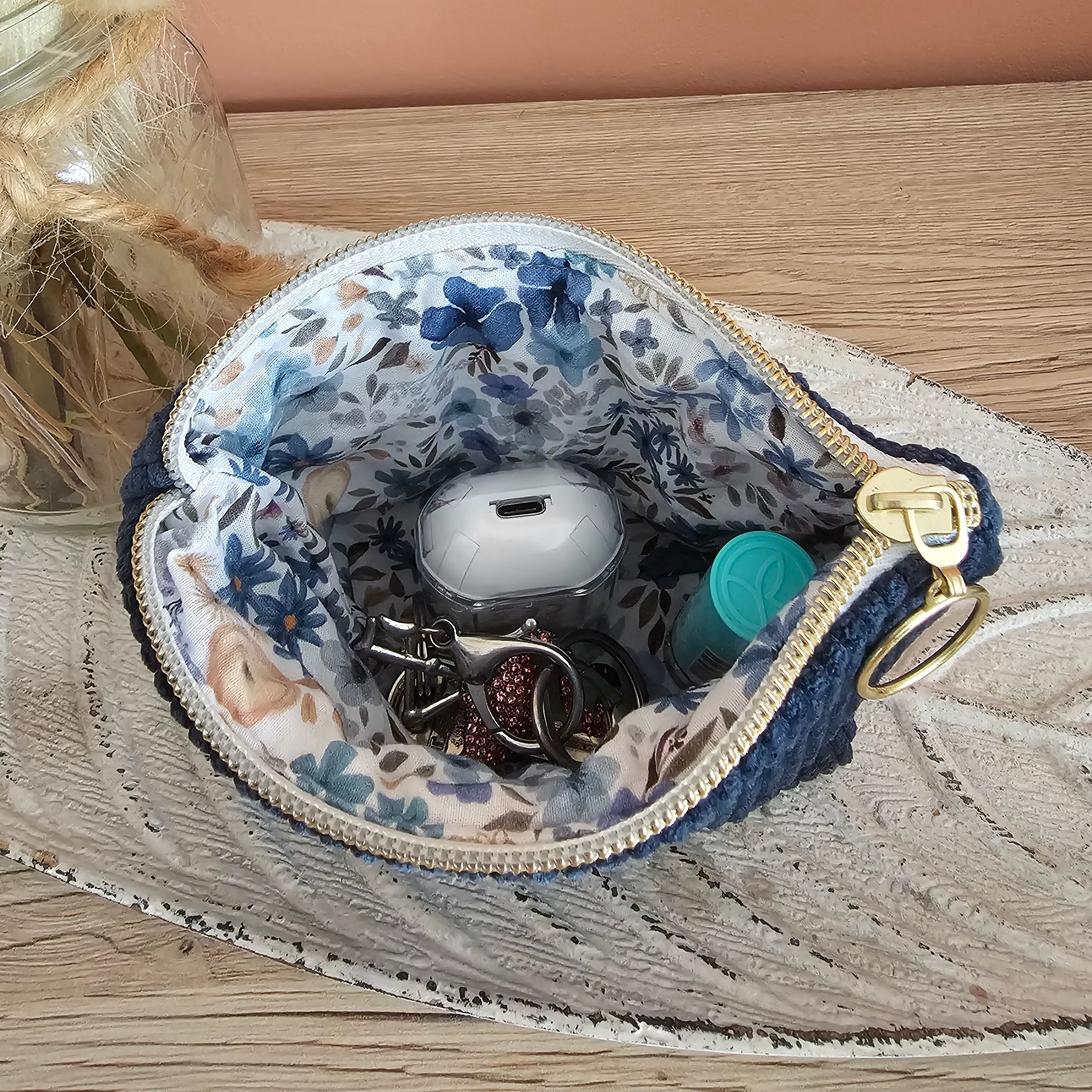 Mini pochette zippée ouverte contenant des écouteurs, baume à lèvre et clés 