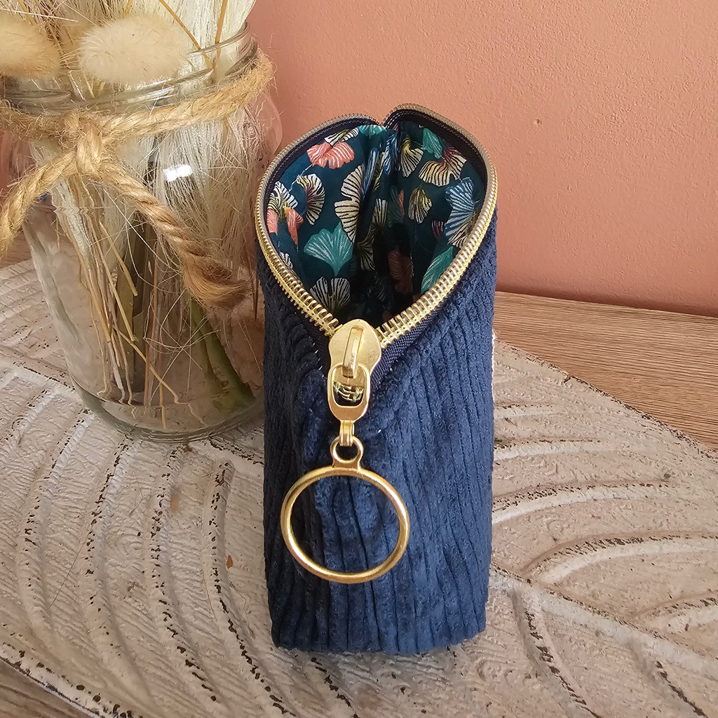 Petite pochette porte monnaie posé sur un meuble en bois. Couleur bleu en velours et coton imprimé ginkgo un zip doré pour une finition élégante 