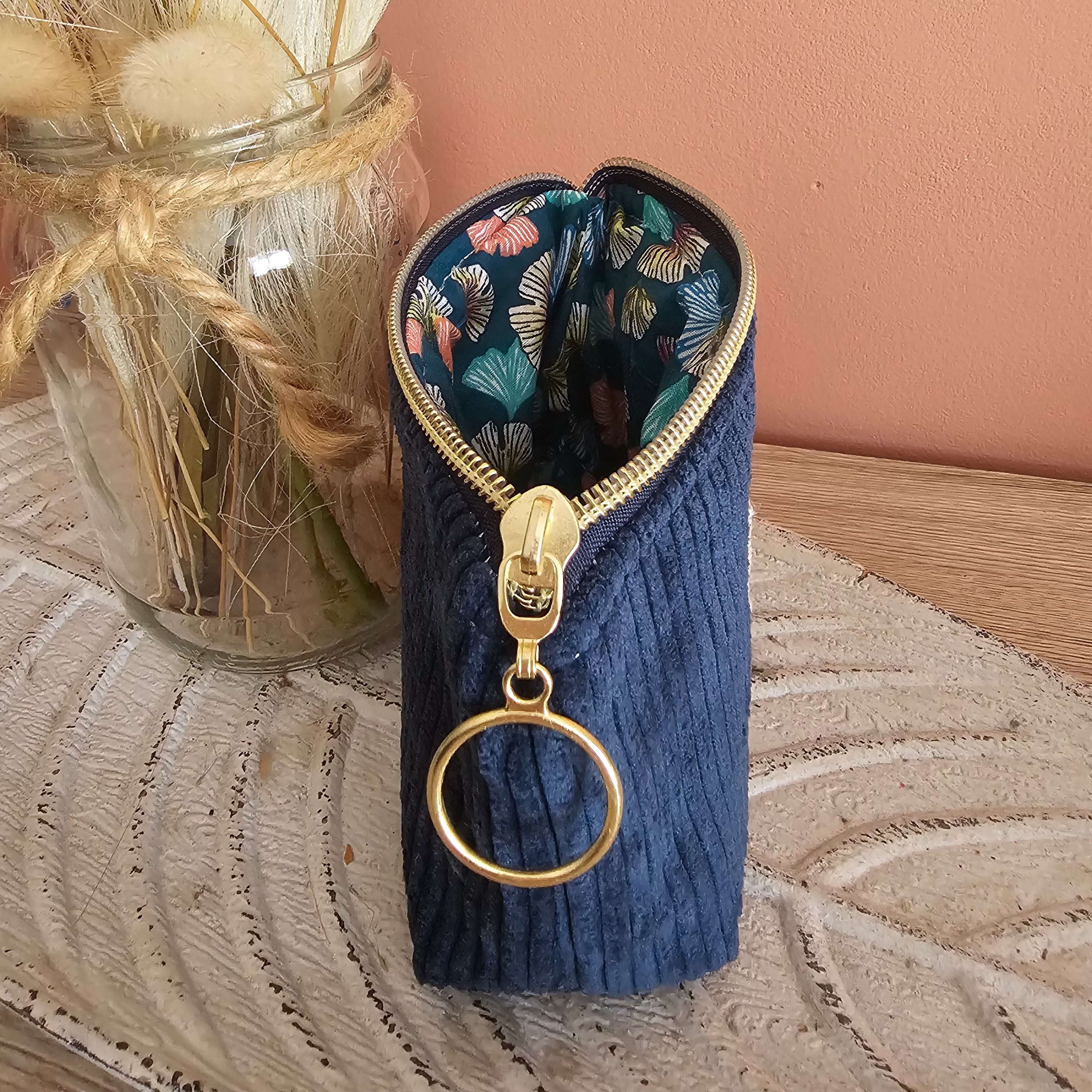 Petite pochette porte monnaie posé sur un meuble en bois. Couleur bleu en velours et coton imprimé ginkgo un zip doré pour une finition élégante 