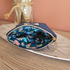 Vue sur l'intérieur de la mini pochette zippée qui est ouverte. Couleur bleu denim en velours à l'extérieur et coton bleu canard à motif ginkgo multicolores pastel à l’intérieur. Posé sur un meuble en bois avec une déco cocooning et douce de fleur sechée 