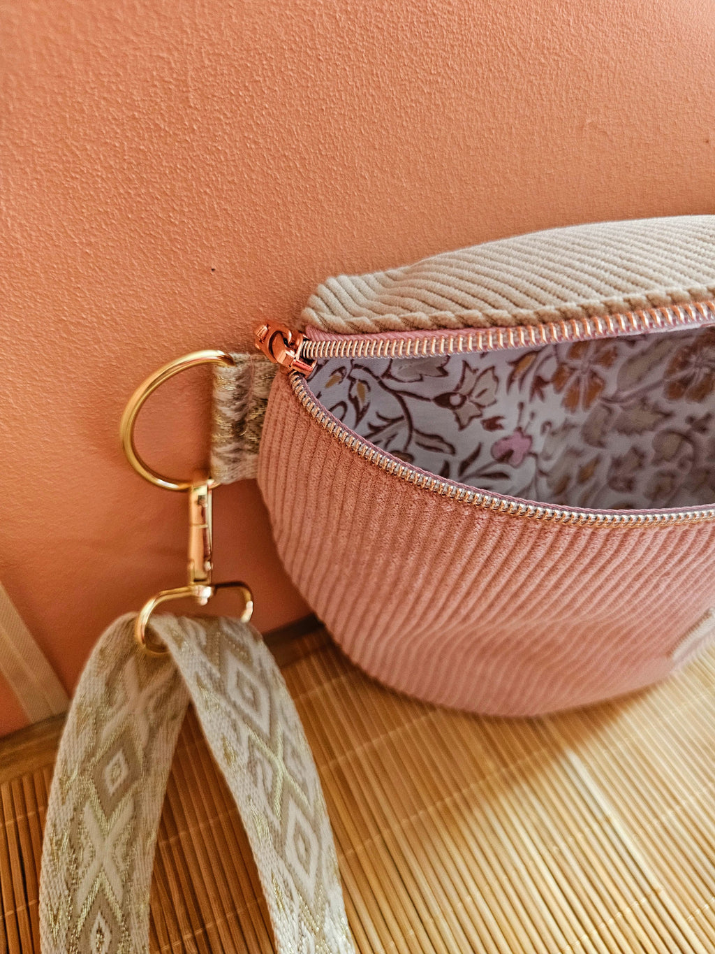 Zoom sur un sac banane entre ouvert en velours cotelé beige et rose. Interieur en coton motif indien pastel. Mercerie doré et bandoulière beige et écru