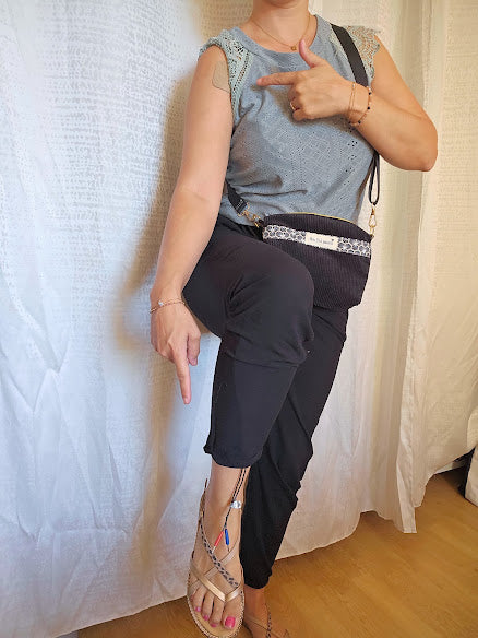 Femme portant le sac bandoulière TENS et montrant l'emplacement des électrodes aux niveaux de l'épaule et sur la jambe. Aucun fil ne l'a gêne et les cables sont cachés 