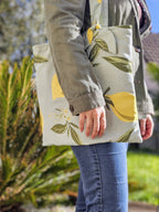 Femme portant un tote bag avec des citrons dessus se promène dans un parc vêtue d'un jean et d'un coupe vent kaki