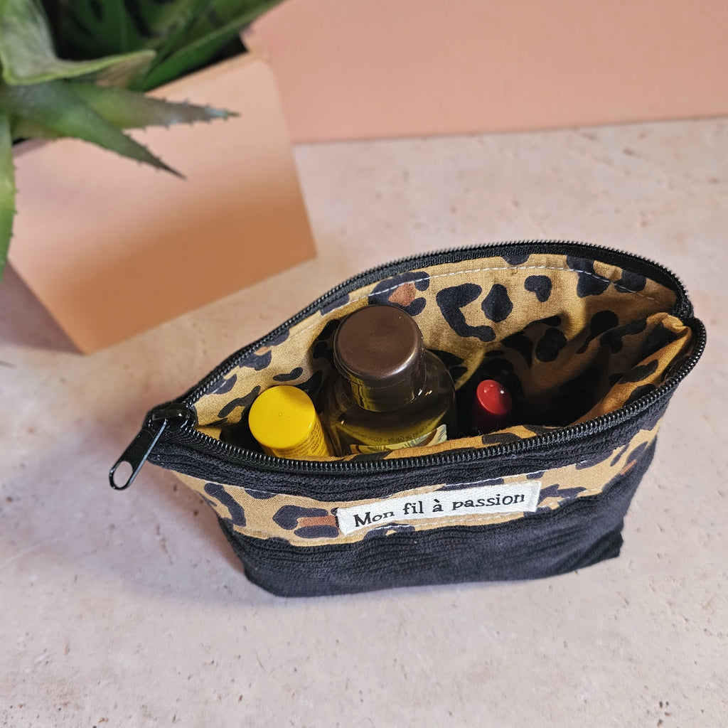 Zoom sur le contenu de la petite pochette contenant un baume a levre une boite de mesicament un petit parfum un désinfectant pour les mains. Porte monnaie en velours côtelé noir et léopard 