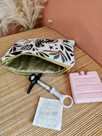 Pochette posée sur une table. Contient un médicament type piqûre injection qui nécessite d'être conserver au frais lors des transports ou voyage. Un bloc de glace et une compresse désinfectante. Trousse isotherme médicale au couleur beige et bleu et motif mystique. Coton enduit doré.