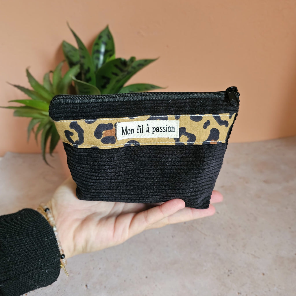 Petite pochette en velours côtelé noir et coton imprimé léopard tenue dans le creux de la main pour montrer son format compact