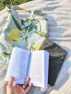 Femme installé sur une couverture de pique nique avec un livre et son tote bag citron contient une gourde et une housse protectrice pour livre Mon Fil à Passion 