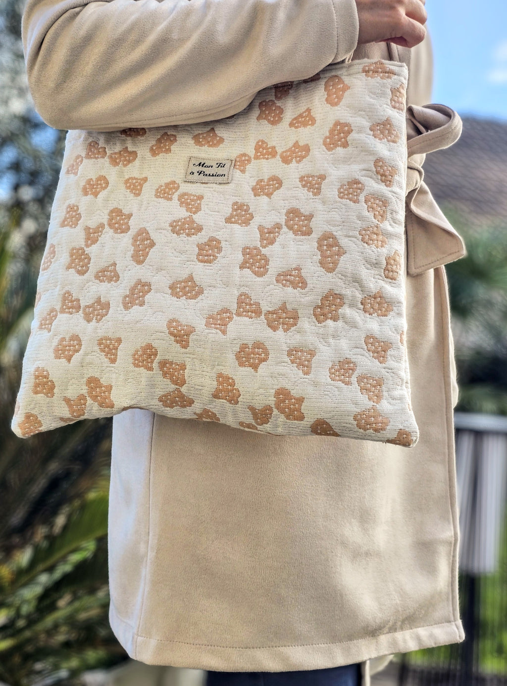 Tote bag au couleur beige et corail pastel porté sur un imper en suédine beige. La femme qui le porte se balade dans un parc 
